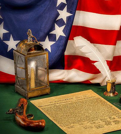 A lantern, quill, flintlock pistol, and parchment resting before an American flag